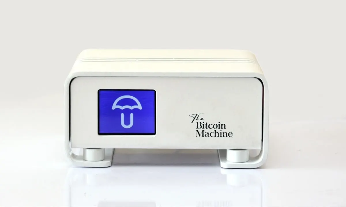 A white Umbrel Bitcoin node, labelled The Bitcoin Machine, with a blue screen